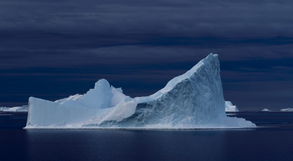 A stark white iceberg against a deep blue still ocean