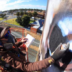 jimmy (DVATE) suspended high in the air, working on a silo mural.