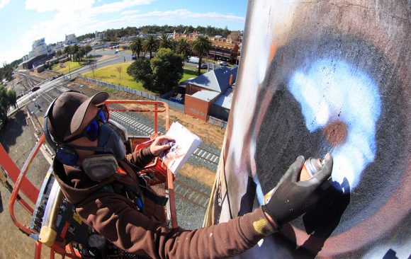jimmy (DVATE) suspended high in the air, working on a silo mural.
