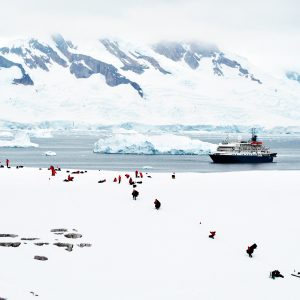 Antarctic tourists and their icebreaker are dwarfed by massive ice mountains in a sea of white.