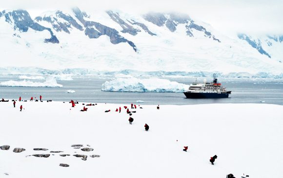Antarctic tourists and their icebreaker are dwarfed by massive ice mountains in a sea of white.